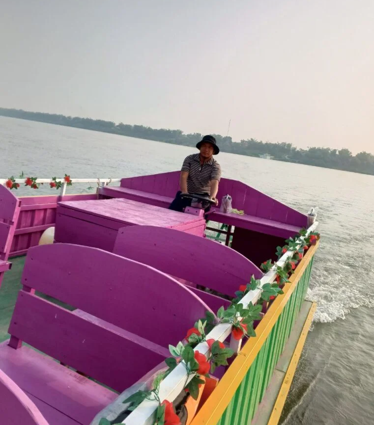 Founder Phonh driving a pink tour boat on the Mekong River for Dream Garden guests.