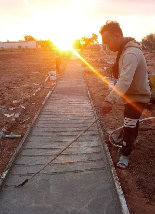 Founder of Dream Garden finishing a DIY concrete walkway during sunset to save construction costs.