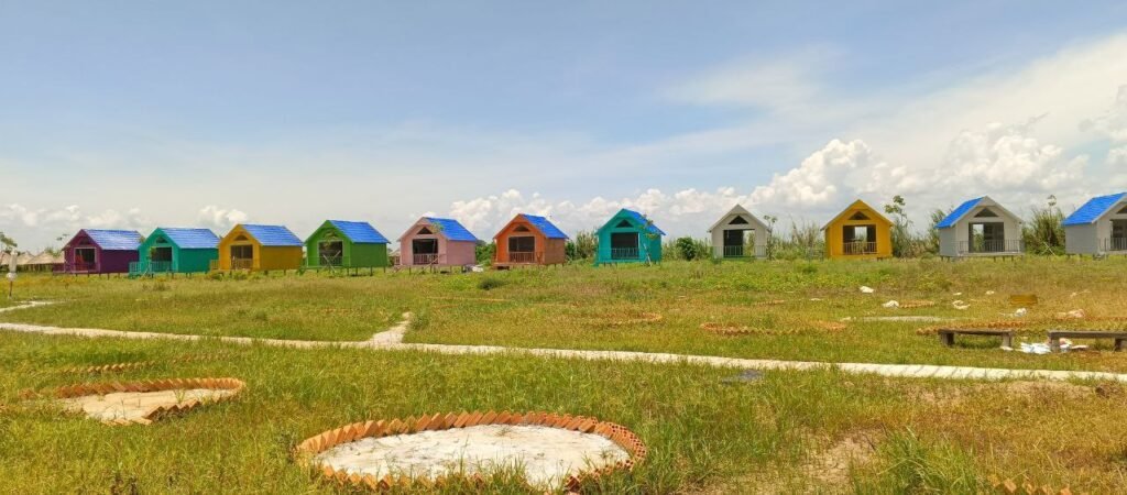Row of small colorful A-frame resort cabins painted blue, orange, and green in a field.