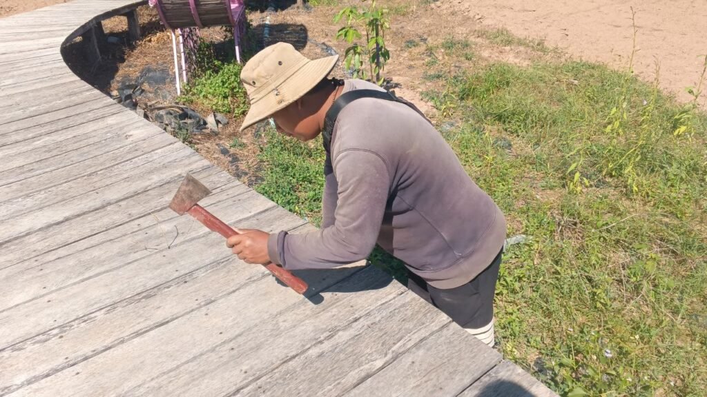 Close-up of Phonh repairing the wooden walkway by hand, illustrating the hard work and grit required to overcome failure.